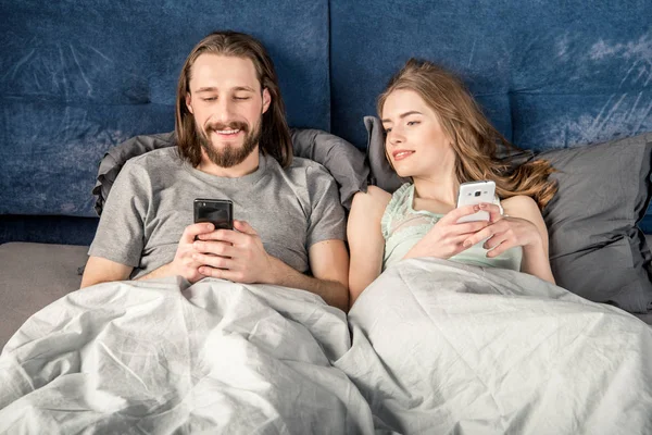 Couple au lit avec smartphones — Photo de stock