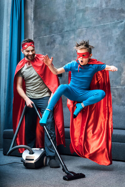 father and son in superhero costumes vacuuming 