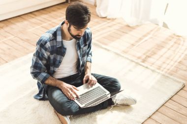 Man sitting on carpet and typing on laptop clipart