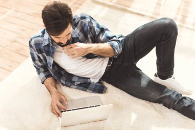 man lying on carpet and using laptop clipart