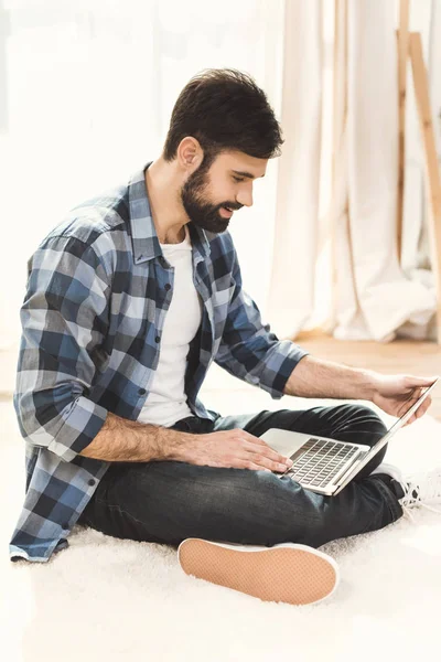 Hombre sentado en la alfombra y trabajando en el ordenador portátil — Foto de Stock