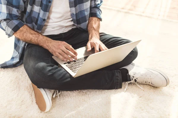 Человек сидит на ковре и печатает на ноутбуке — стоковое фото