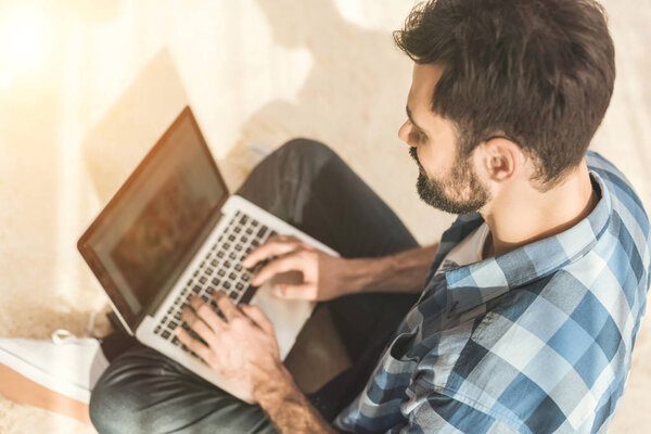 Man sitting on carpet and typing on laptop