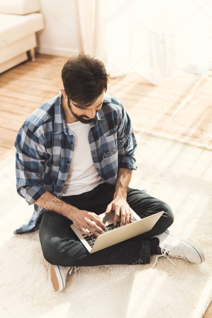 Man sitting on carpet and typing on laptop
