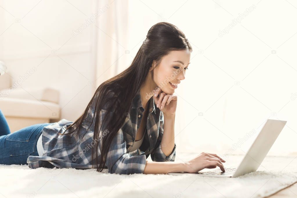 woman lying on carpet and using laptop