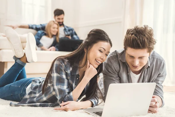 Casal deitado no tapete e usando laptop — Fotografia de Stock