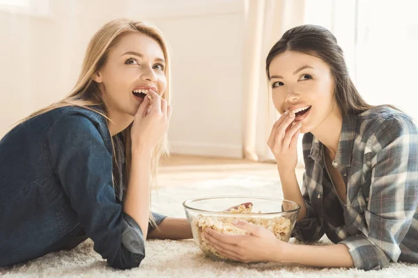 Žen, které leží na koberci a jíst popcorn — Stock fotografie