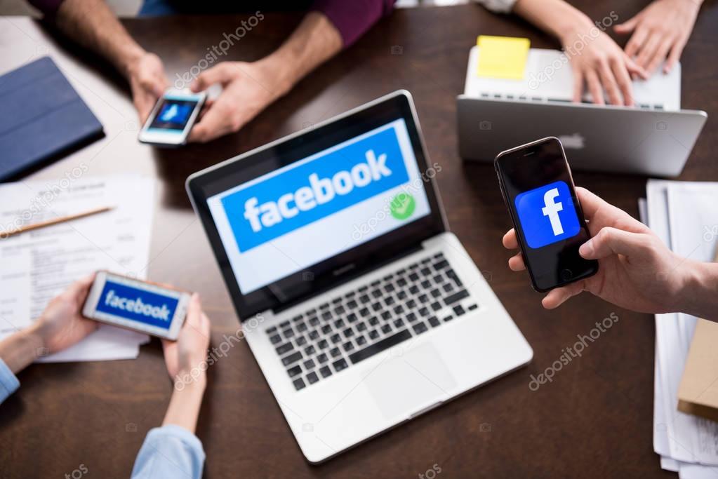 Cropped shot of businesspeople using digital devices with facebook logo icons on screens