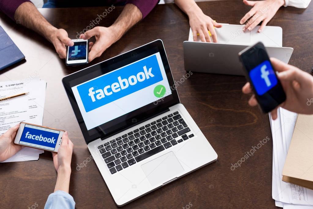 Cropped shot of businesspeople using digital devices with facebook logo icons on screens