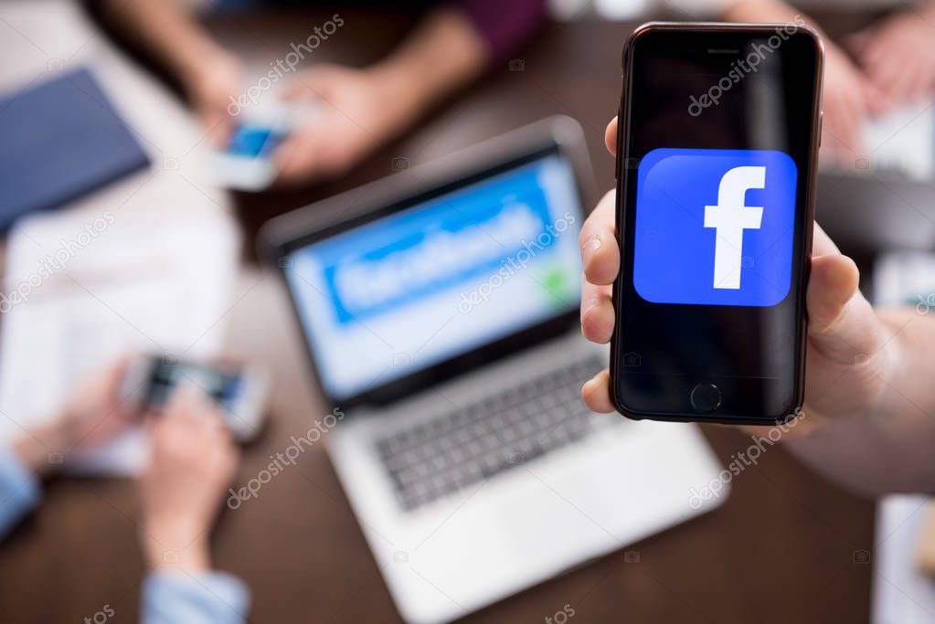 Close-up partial view of hand holding smartphone with facebook logo icon on screen