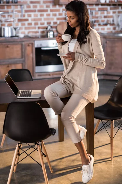 Женщина пьет кофе и пользуется ноутбуком — стоковое фото