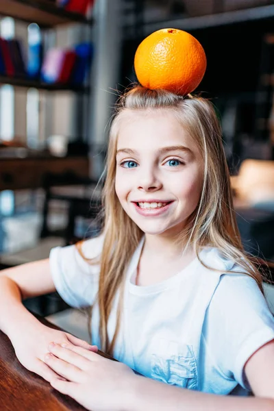 Χαμογελαστό παιδί κορίτσι με πορτοκάλι στο κεφάλι — Φωτογραφία Αρχείου