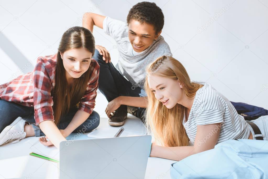 multiethnic smiling teenagers with laptop