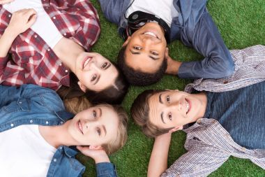 multiethnic teenagers lying on green lawn