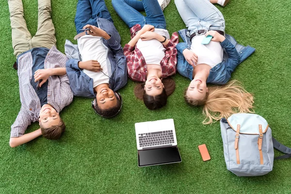 Multietniskt tonåringar vilar på grön gräsmatta — Stockfoto