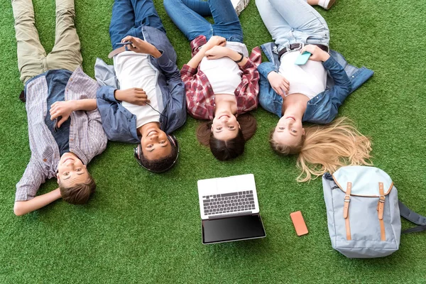 Adolescentes multiétnicos descansando en el césped verde —  Fotos de Stock