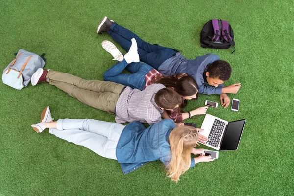 Багатонаціональні підлітки з ноутбуком на зеленому газоні — стокове фото