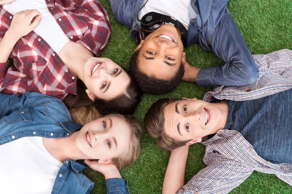 Adolescentes multiétnicos deitados no gramado verde — Fotografia de Stock