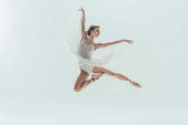 junge elegante Ballerina im weißen Kleid springt im Studio, isoliert auf Weiß