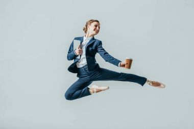 businesswoman in suit and ballet shoes jumping with coffee and digital tablet, isolated on grey clipart