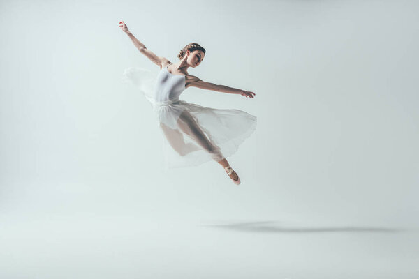 elegant ballet dancer in white dress jumping in studio, isolated on white