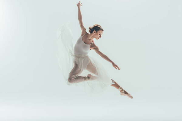 beautiful ballet dancer in white dress jumping in studio, isolated on white