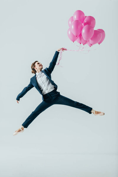 businesswoman in suit and ballet shoes jumping with pink balloons, isolated on grey