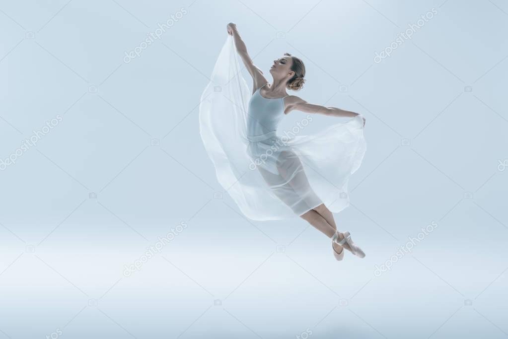 elegant ballet dancer in white dress jumping in studio, isolated on white