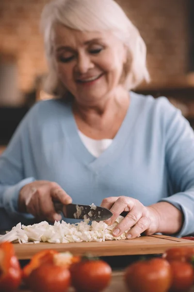 Пожилая женщина режет лук — стоковое фото