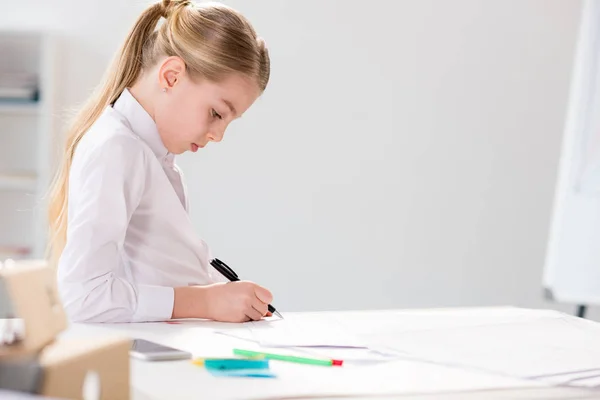 Серйозна маленька дівчинка, що пише за столом — стокове фото