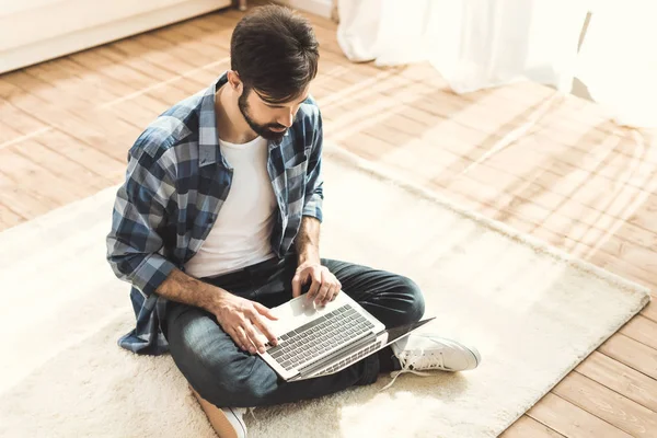 Homem sentado no tapete e digitando no laptop — Fotografia de Stock