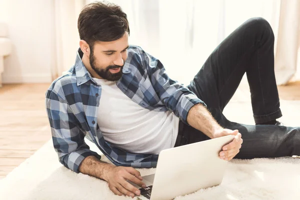 Mann liegt auf Teppich und benutzt Laptop — Stockfoto