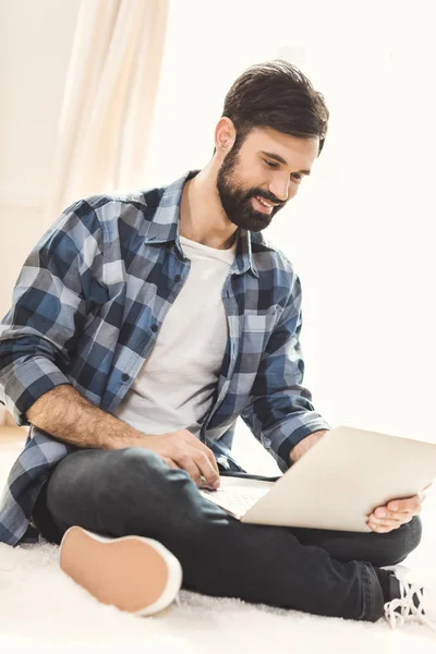 Man sitting on carpet and using laptop — Stock Photo