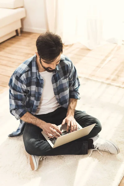 Homem sentado no tapete e digitando no laptop — Fotografia de Stock