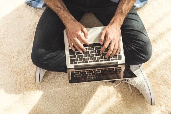 Hombre sentado en la alfombra y escribiendo en el ordenador portátil — Stock Photo