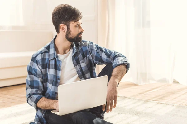 Thoughtful man sitting on carpet and daydreaming — Stock Photo