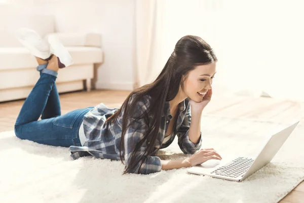 Frau liegt auf Teppich und benutzt Laptop — Stockfoto