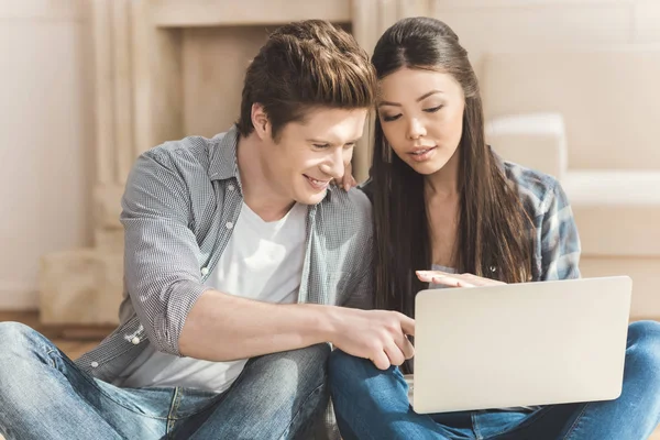 Pareja sentada en el suelo y mirando el ordenador portátil - foto de stock