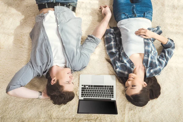 Coppia sdraiata sul tappeto tra laptop — Foto stock