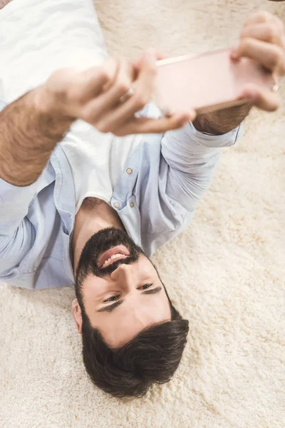 Homem tomando selfie enquanto deitado no tapete — Fotografia de Stock