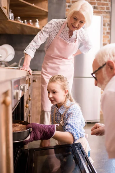 Chica colocando pastel en el horno - foto de stock