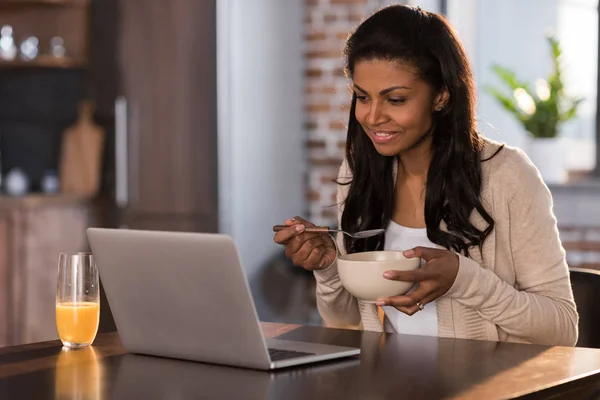 Mujer desayunando y usando laptop - foto de stock