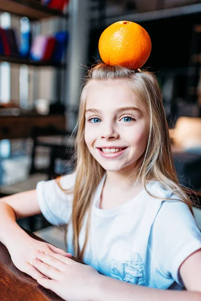 Smiling kid girl with orange on head — Stock Photo