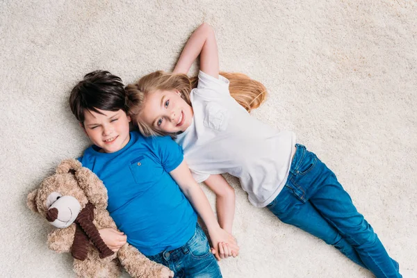 Niño y niña acostados en la alfombra - foto de stock