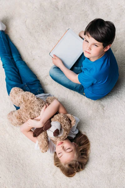 Girl with teddy bear and boy with tablet — Stock Photo
