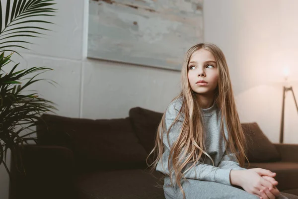 Pensive kid girl sitting on sofa — Stock Photo
