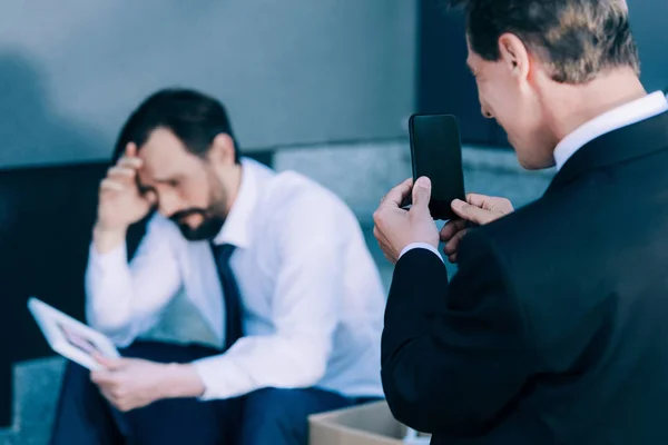 Hombre de negocios con teléfono inteligente fotografiando colega despedido - foto de stock