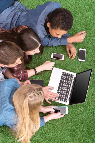 Multiethnic teenagers with laptop on green lawn — Stock Photo