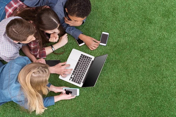 Adolescents multiethniques avec ordinateur portable sur pelouse verte — Photo de stock