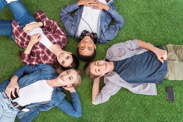 Многонациональные подростки, лежащие на зеленой лужайке — стоковое фото